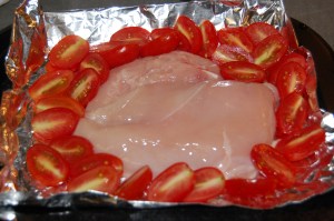 Organic grape tomatoes around skinless, boneless chicken breast half.